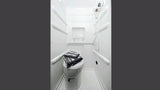 Compact white RV rental bathroom with toilet, wall-mounted shower, and shelf. Towels are neatly folded on the toilet.