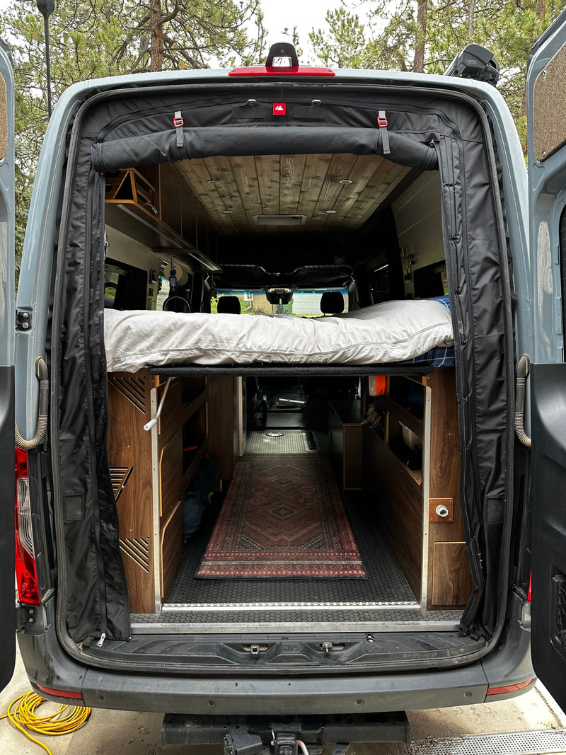 Step into your next rv rental adventure! Rear view of a custom camper van interior with a raised bed, storage, and cozy rug. — photo 11