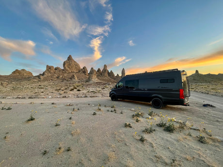 Exploring the desert with an RV rental! Dark camper van amidst unique rock formations under a vibrant sunset sky.