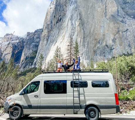Joyful family on an RV rental van's roof, arms raised, against Yosemite's majestic El Capitan. Epic van life!