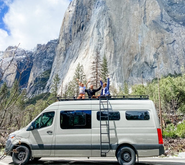 Joyful family on an RV rental van's roof, arms raised, against Yosemite's majestic El Capitan. Epic van life!