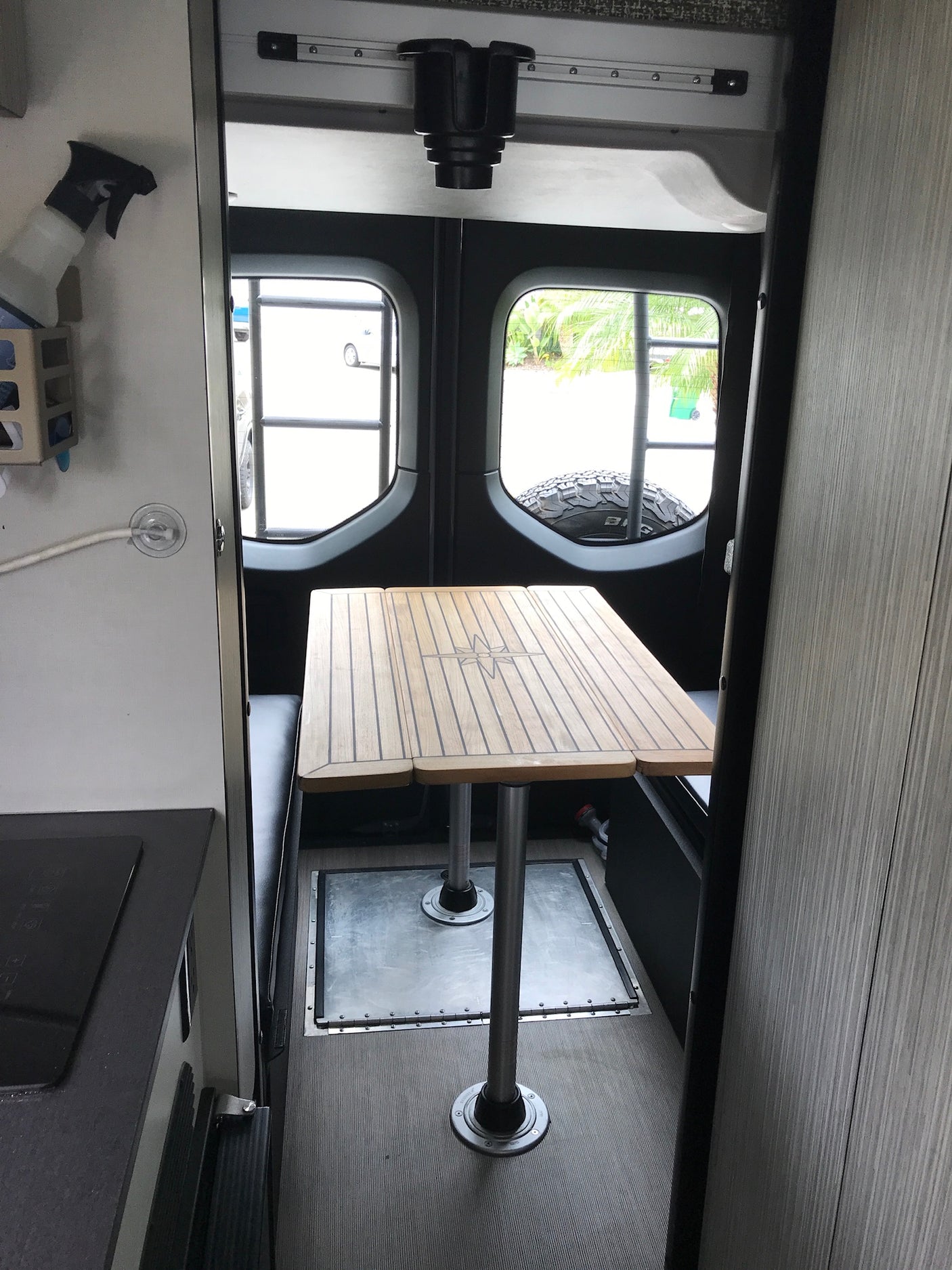RV rental interior: Wooden dining table with compass design, built-in benches & compact kitchen ready for adventure.