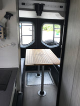 RV rental interior: Wooden dining table with compass design, built-in benches & compact kitchen ready for adventure.