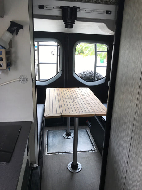 RV rental interior: Wooden dining table with compass design, built-in benches & compact kitchen ready for adventure.