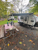 RV rental teardrop camper with awning & picnic table at a fall campsite among colorful leaves.