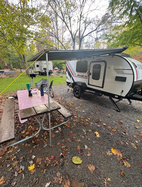 RV rental teardrop camper with awning & picnic table at a fall campsite among colorful leaves.