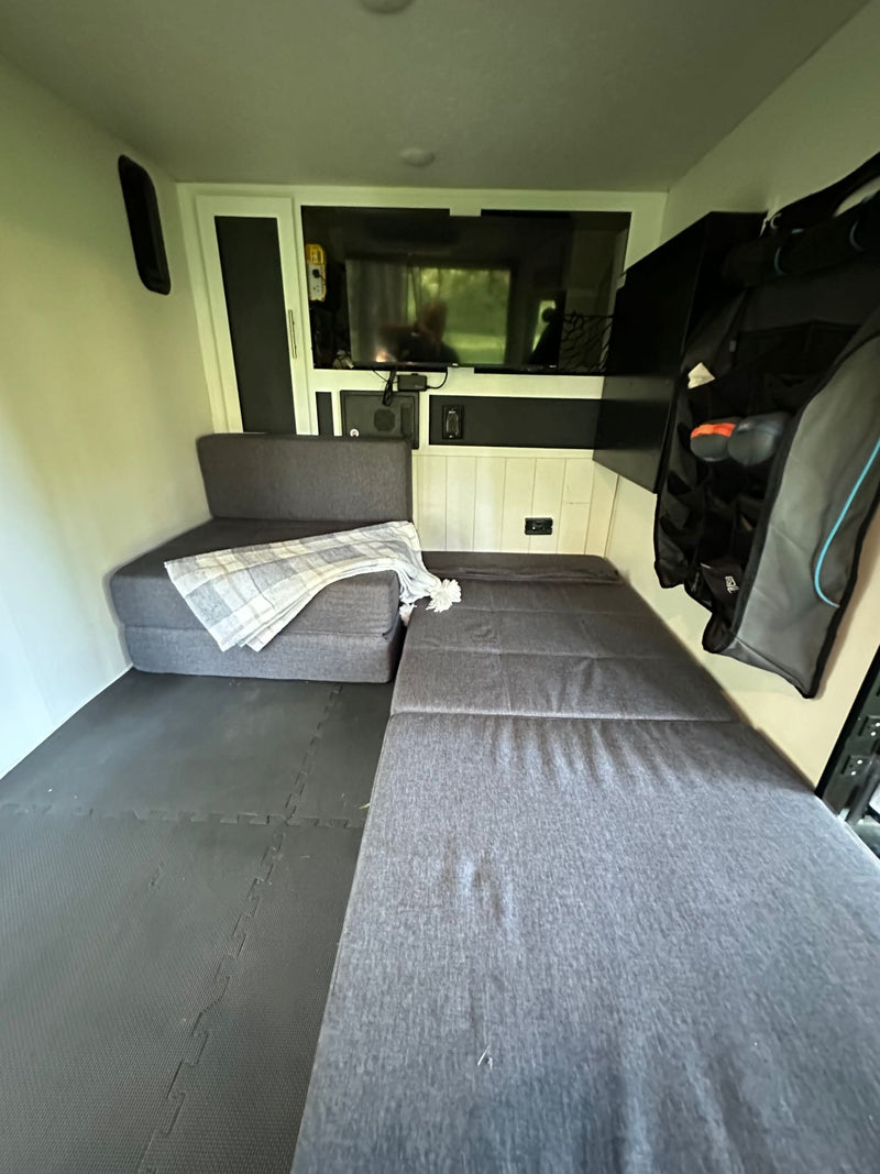 Compact RV rental interior: modular seating converts to a bed, with TV and hanging storage. — photo 11