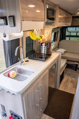Inside an RV rental: a modern, compact kitchenette with sink, induction cooktop, microwave, and rear seating area.