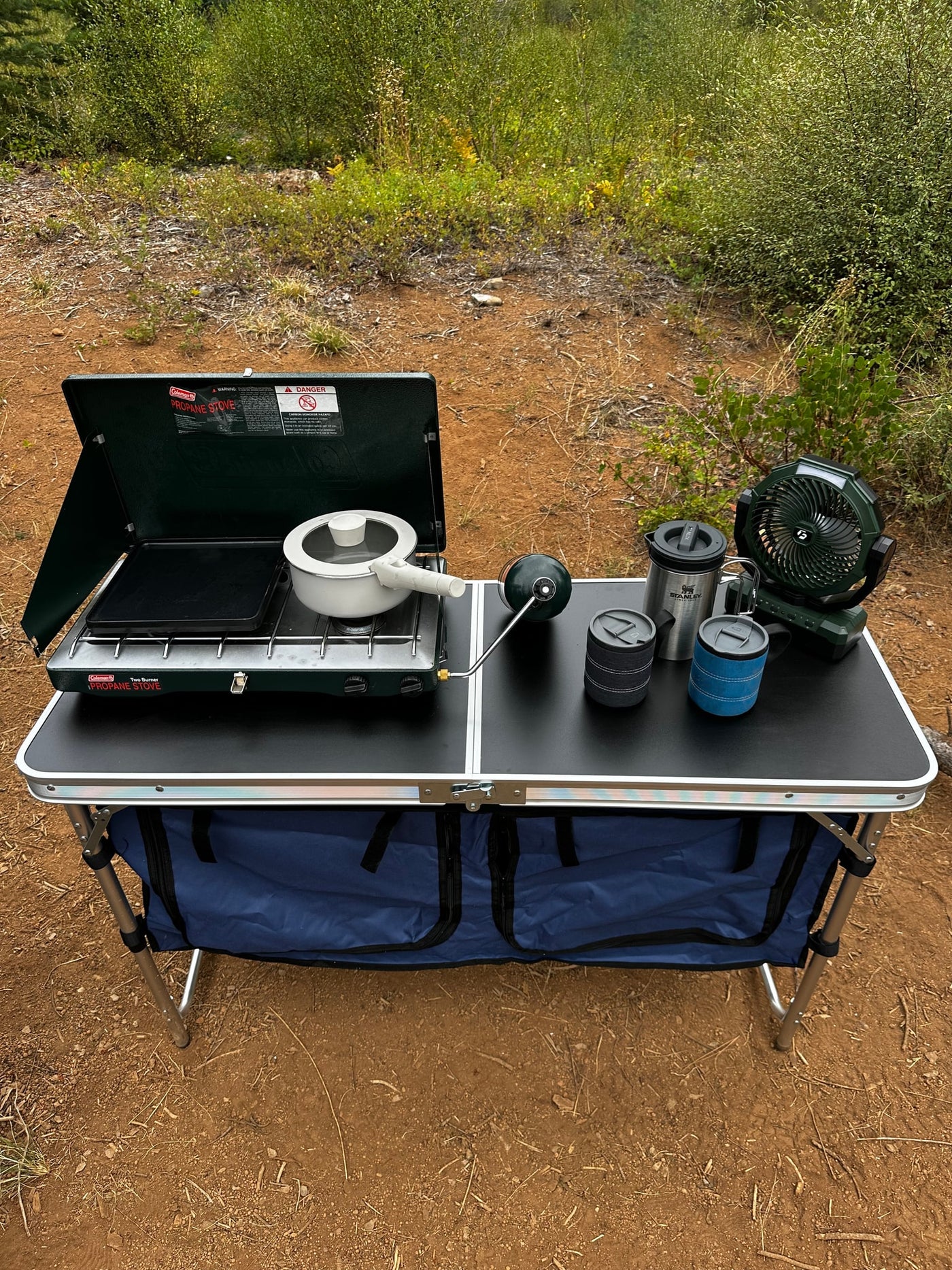 RV rental ready: Portable camping kitchen setup with a Coleman stove, pot, griddle, fan, and mugs on a folding table. — photo 15