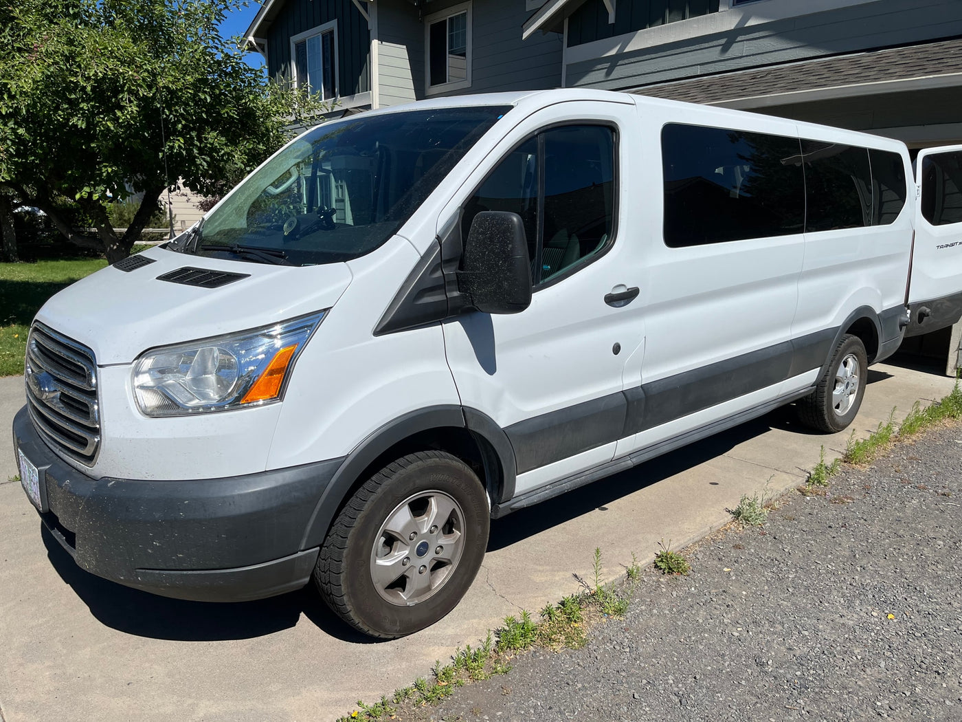 White Ford Transit passenger van, often used for RV rental adventures, parked on a sunlit driveway next to a house and tree. — photo 4