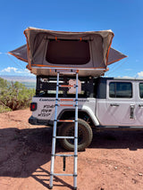 Explore with this RV rental: White Jeep Gladiator with deployed roof-top tent and ladder, ready for off-road camping adventures.