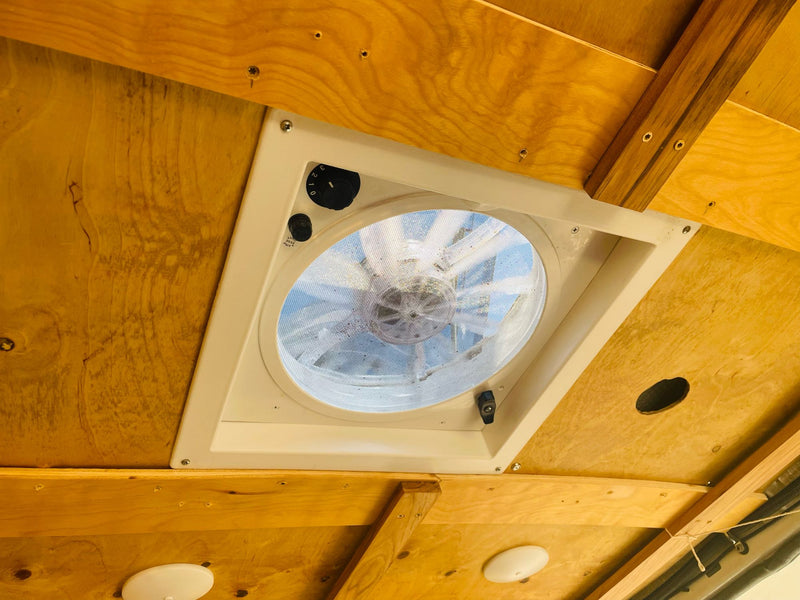 Overhead view in an rv rental: functional ceiling vent fan with adjustable settings, set into a warm wood panel. — photo 12