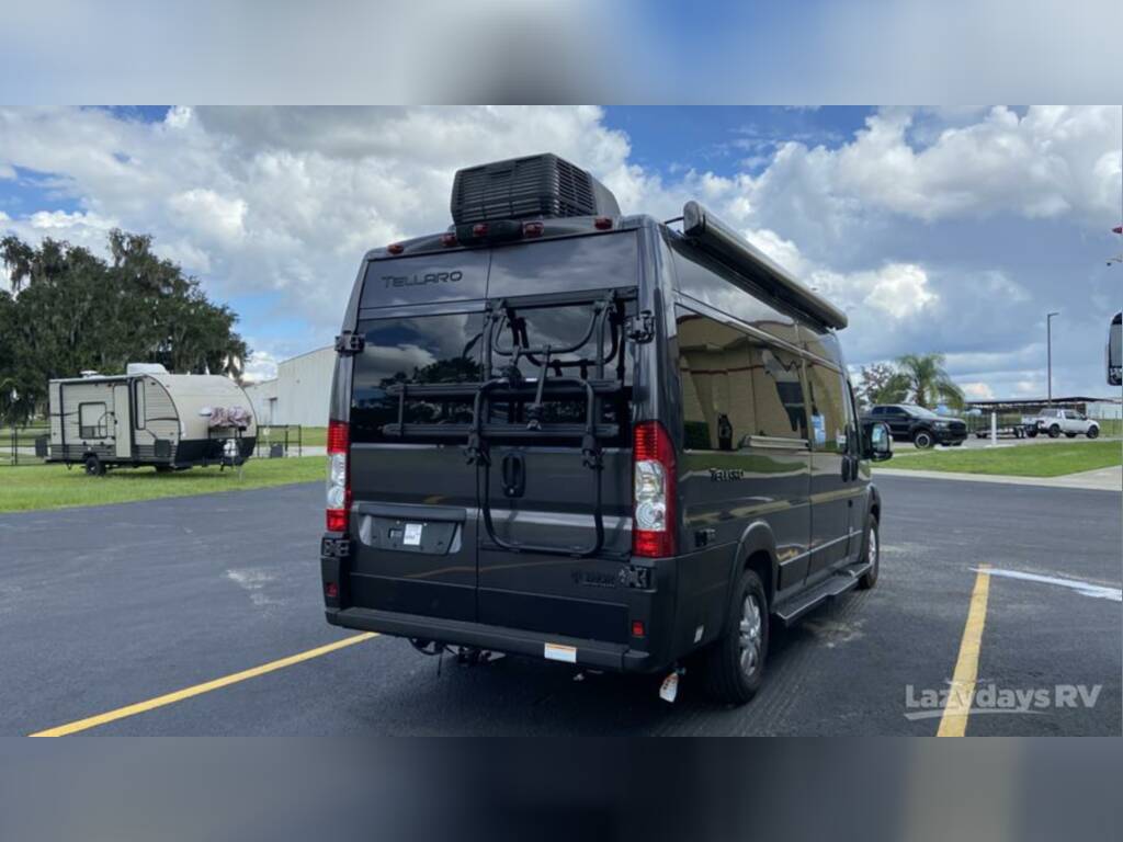 Black Tellaro camper van with bike rack and awning, perfect for RV rental, parked at Lazydays RV. A travel trailer is in the background.