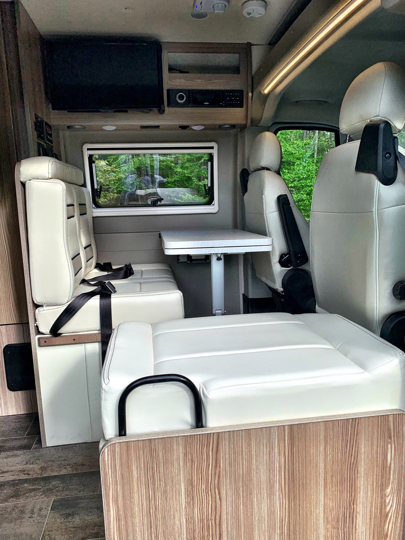 An RV rental's versatile interior featuring light leatherette seating, a convertible dinette table, and entertainment unit. — photo 8