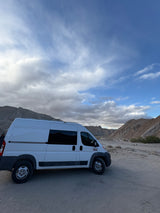 White RV rental van parked in a scenic desert landscape with mountains under a partly cloudy sky.