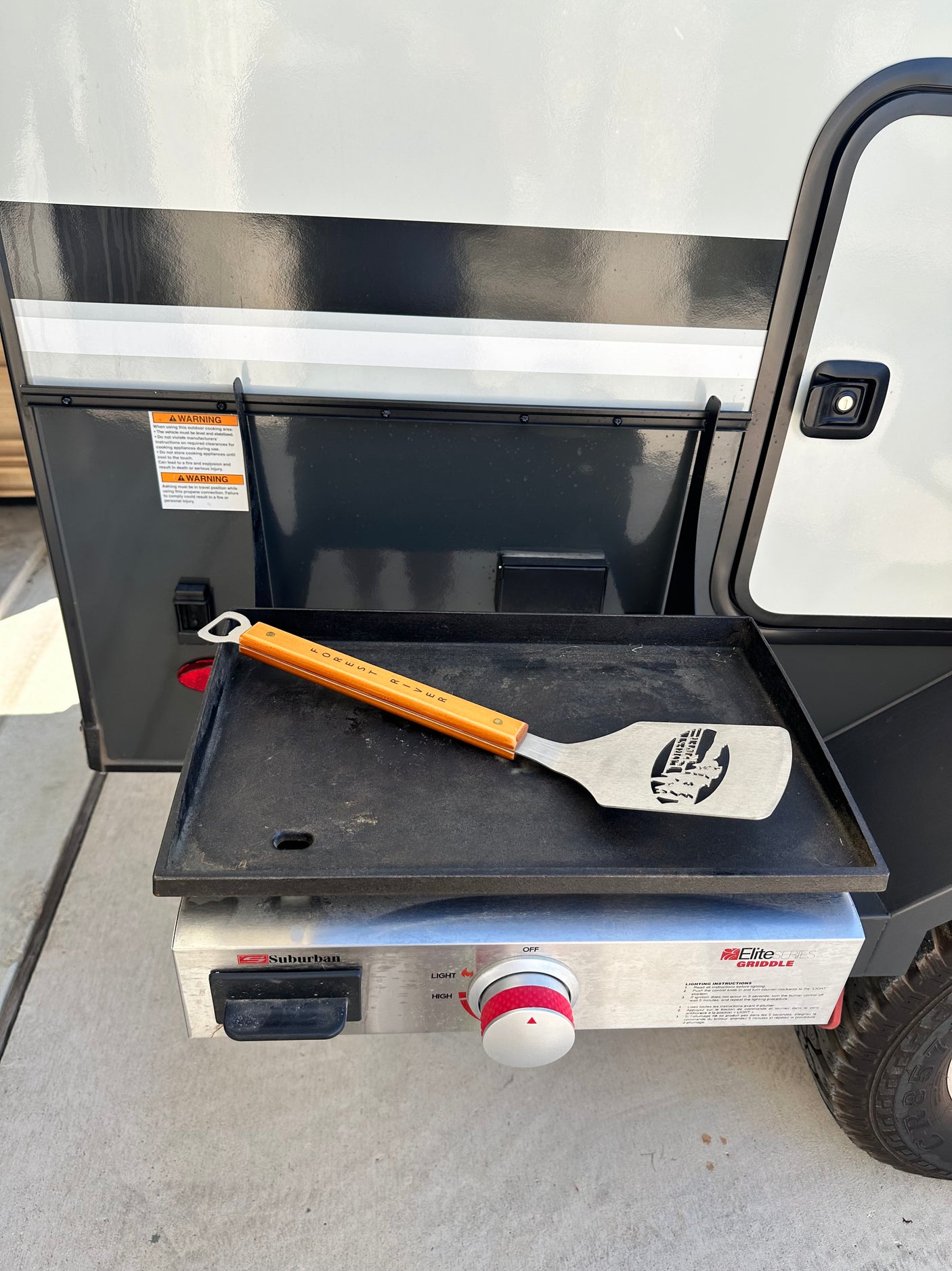 This RV rental features a Suburban griddle and "FOREST RIVER" spatula for easy outdoor cooking, with visible safety warnings.