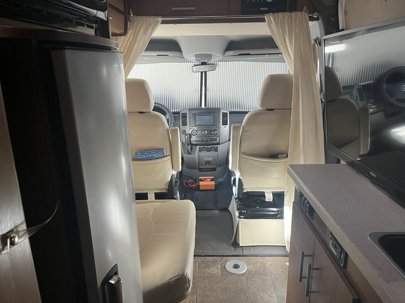 Inside an RV rental, looking forward past a refrigerator and TV towards the front seats and cockpit dashboard. — photo 17