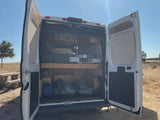 Open rear doors of a white camper van showing its interior bed & storage, ready for adventure. Ideal for an RV rental.