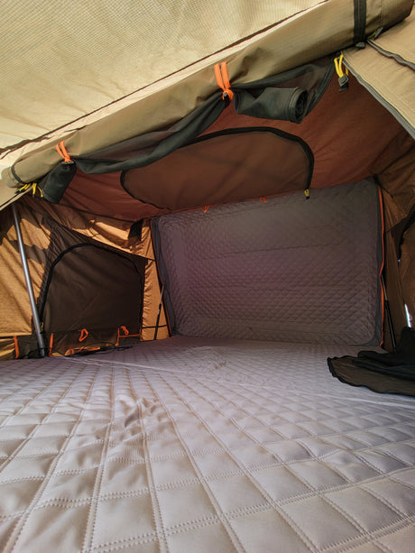 Inside an RV rental's rooftop tent, showcasing a spacious, comfortable quilted mattress and sturdy fabric interior.