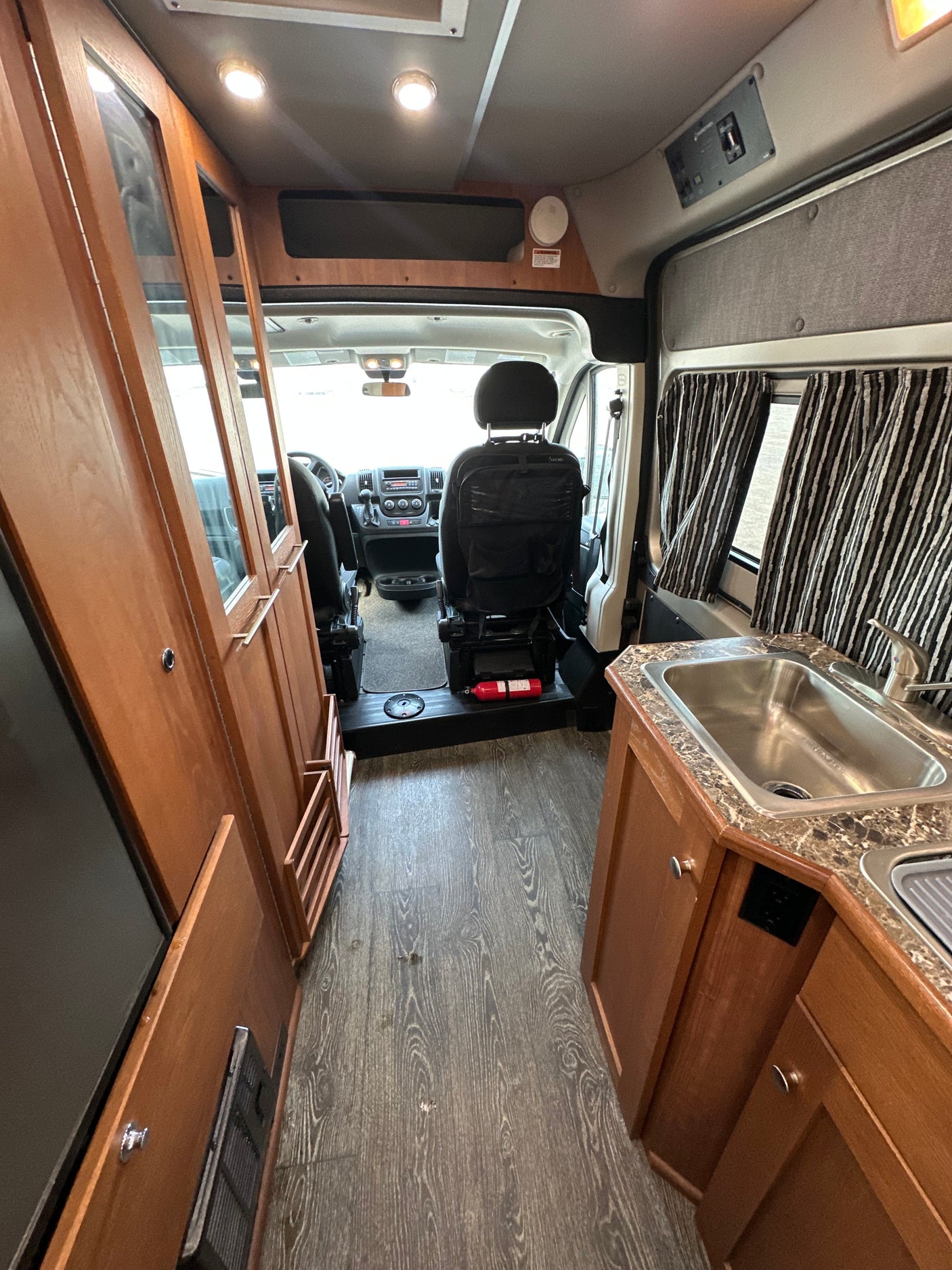 Spacious RV rental interior, showing the driver's cab, a kitchenette with sink, and rich wood cabinetry with laminate flooring.
