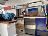 Spacious RV rental kitchen featuring a vibrant blue sink, gas stove, fridge, and ample storage, perfect for your next adventure.