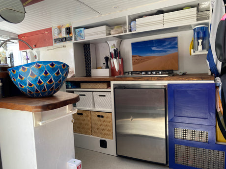 Spacious RV rental kitchen featuring a vibrant blue sink, gas stove, fridge, and ample storage, perfect for your next adventure.
