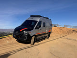 This sleek RV rental, a custom gray Mercedes Sprinter camper van with bold stripes, is ready for adventure on a dirt hilltop.
