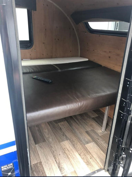 Cozy RV rental interior: brown cushioned bed, wood-paneled walls, and windows. Ideal for road trip comfort.