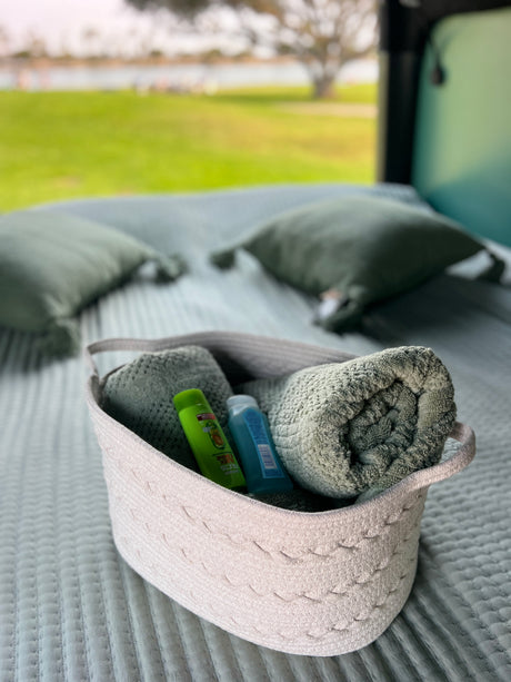 Inside an RV rental: A basket of fresh towels & toiletries rests on a quilted bed, offering comfort with a scenic view.