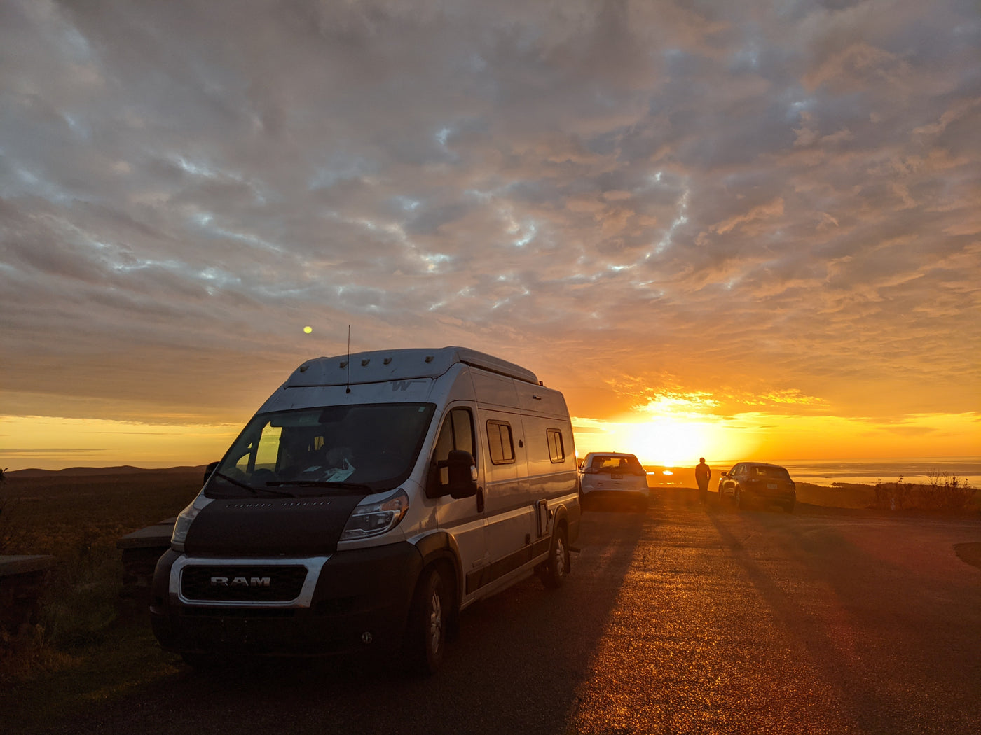 An RV rental basks in the golden light of sunset at a scenic overlook. Distant waters and hills offer a beautiful road trip view. — photo 8