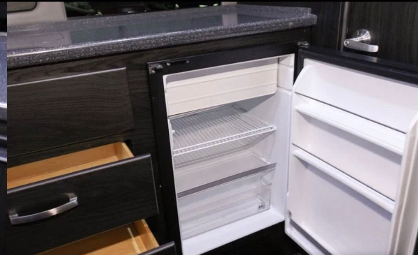 RV rental kitchen interior featuring an open compact fridge, countertop, and drawers. — photo 17