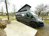 Grey camper van RV rental with pop-top roof deployed, parked at a quiet campground site.