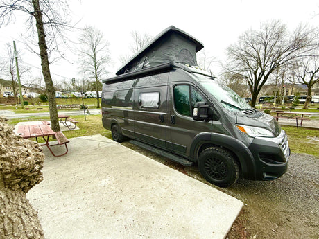 Grey camper van RV rental with pop-top roof deployed, parked at a quiet campground site.