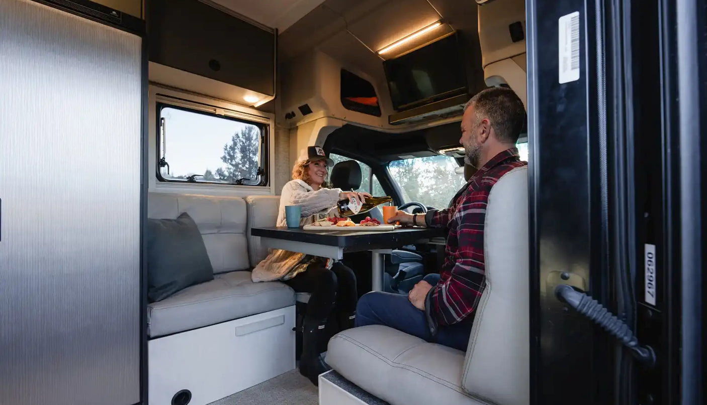 Cozy RV rental interior: A couple enjoys snacks & drinks at a table inside their spacious camper van.