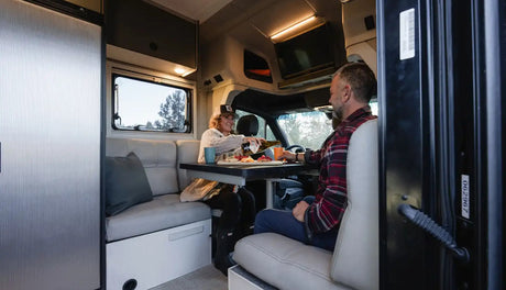 Cozy RV rental interior: A couple enjoys snacks & drinks at a table inside their spacious camper van.