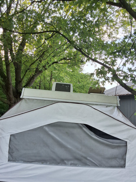 An rv rental pop-up camper's white canvas tent and roof AC unit are set amidst bright green trees, ready for camping.