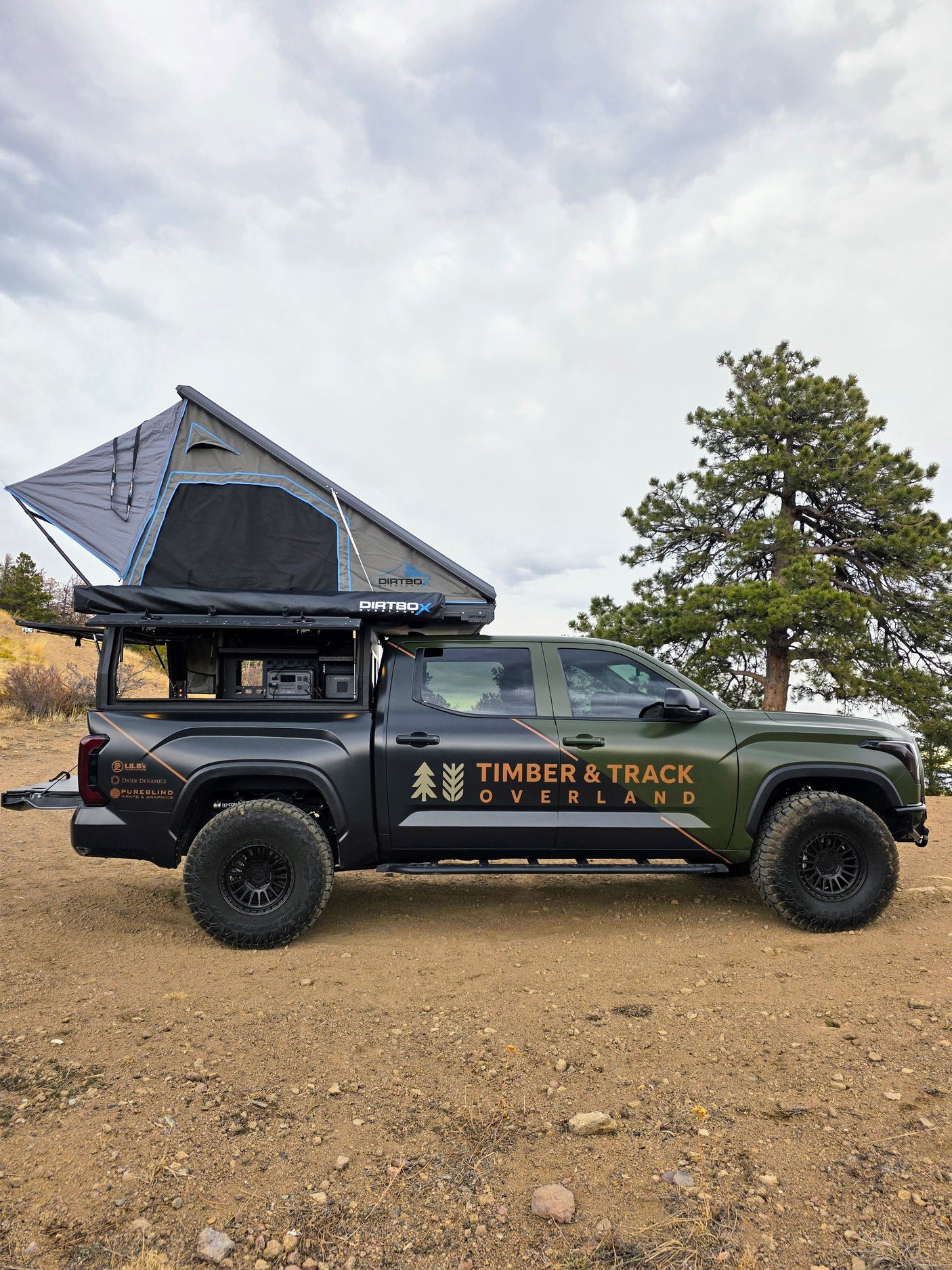 A green & black overland truck, branded 'Timber & Track Overland', with a rooftop tent. An ideal rv rental for off-grid camping.