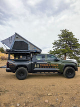 A green & black overland truck, branded 'Timber & Track Overland', with a rooftop tent. An ideal rv rental for off-grid camping.