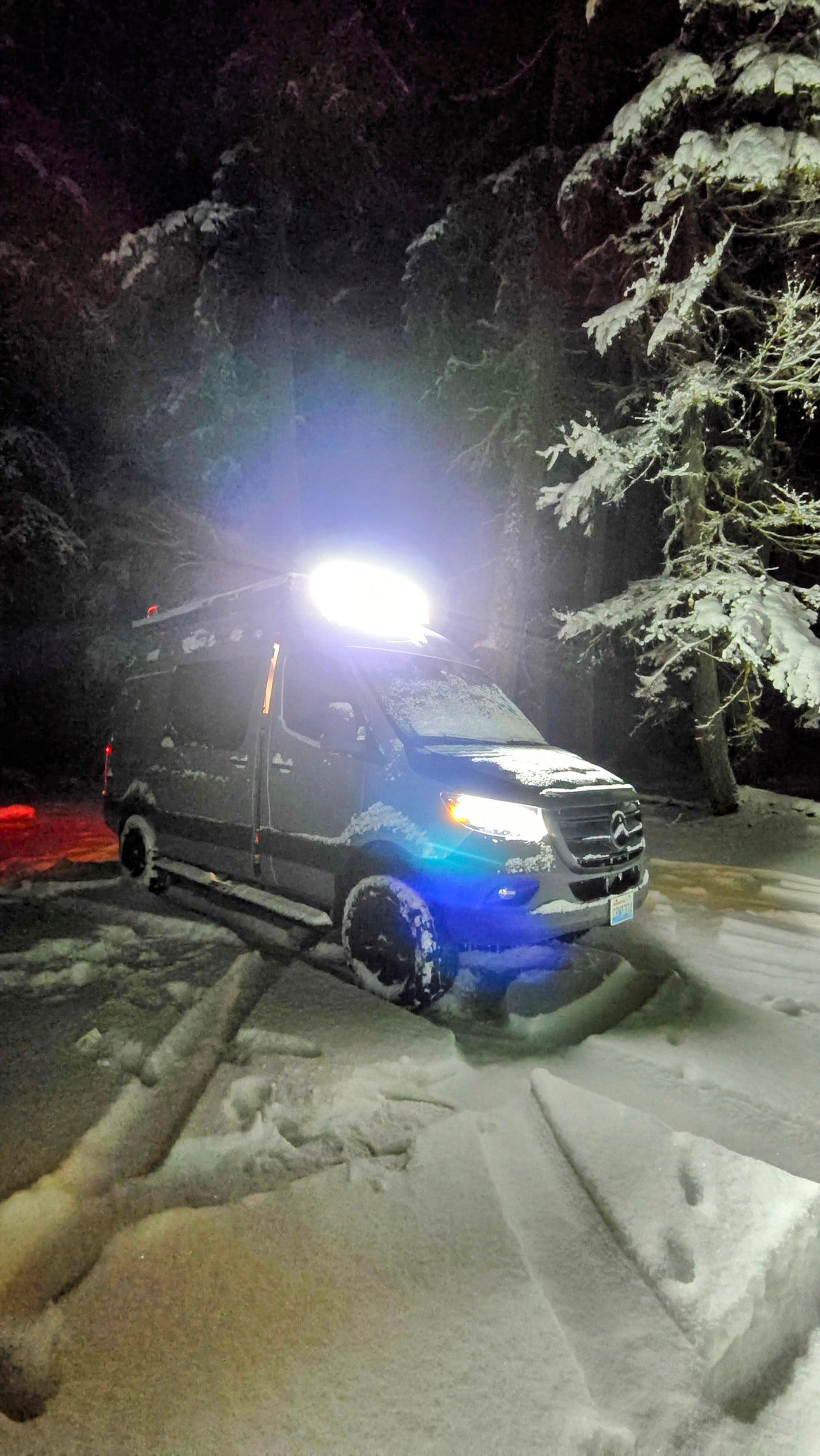 Experience winter van life! This bright RV rental is parked deep in a snowy forest at night, ready for adventure.