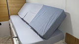 Cozy RV rental bed with light gray sheets and two comfy wedge pillows. Perfect for travel comfort and relaxation.