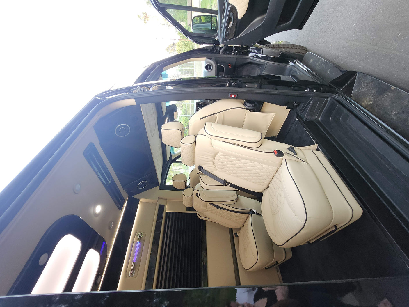 Experience a spacious luxury conversion van interior with cream quilted leather seats and ambient lighting, perfect for RV rental.