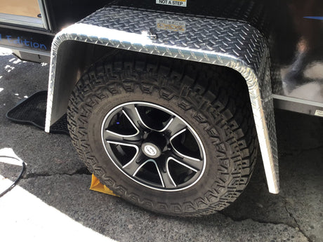 All-terrain tire and diamond plate fender of an RV rental, with a wheel chock. Parked & ready for adventure.