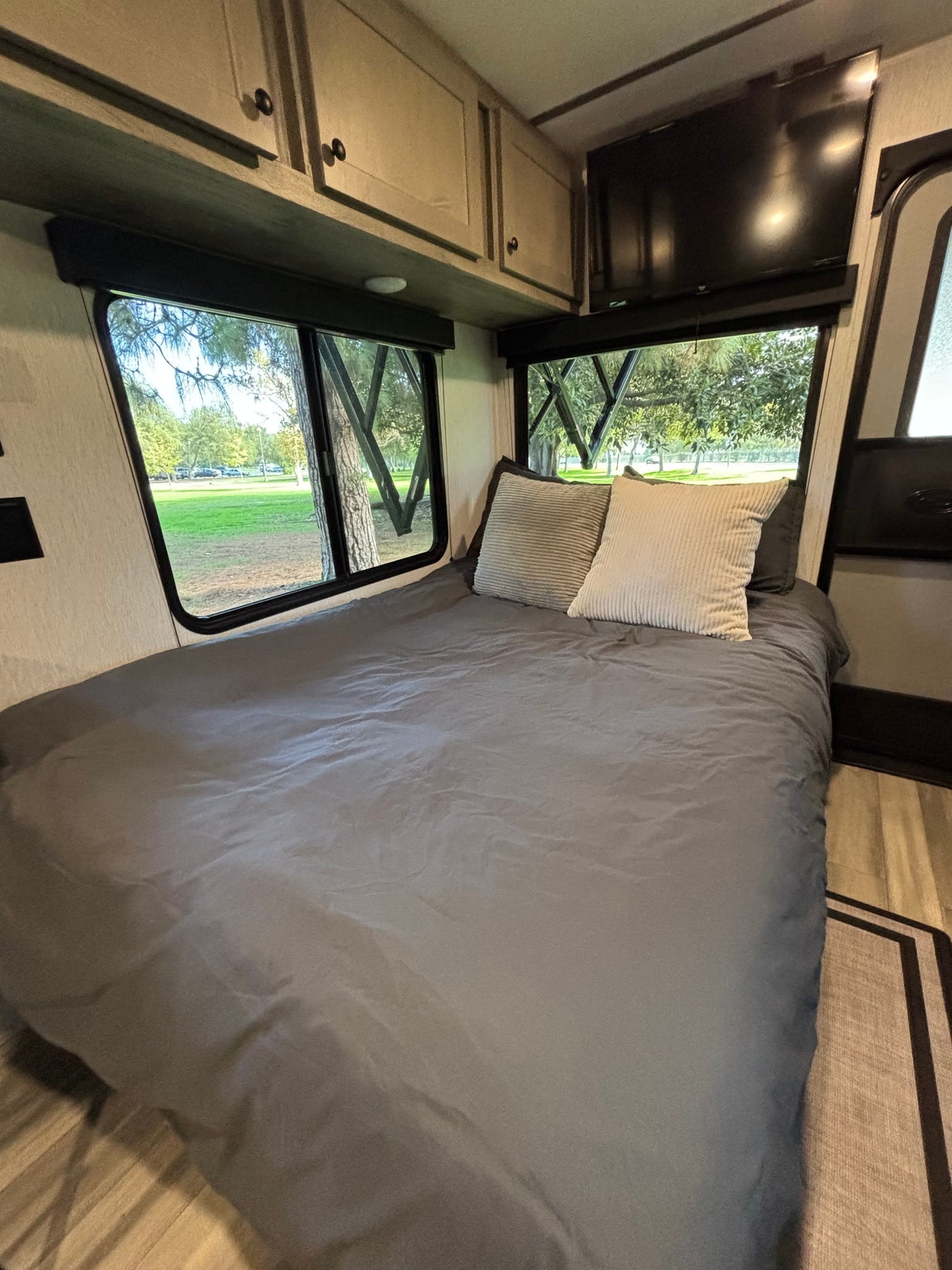 RV rental bedroom: a cozy bed, overhead storage, TV, and large windows revealing a beautiful park setting. — photo 9