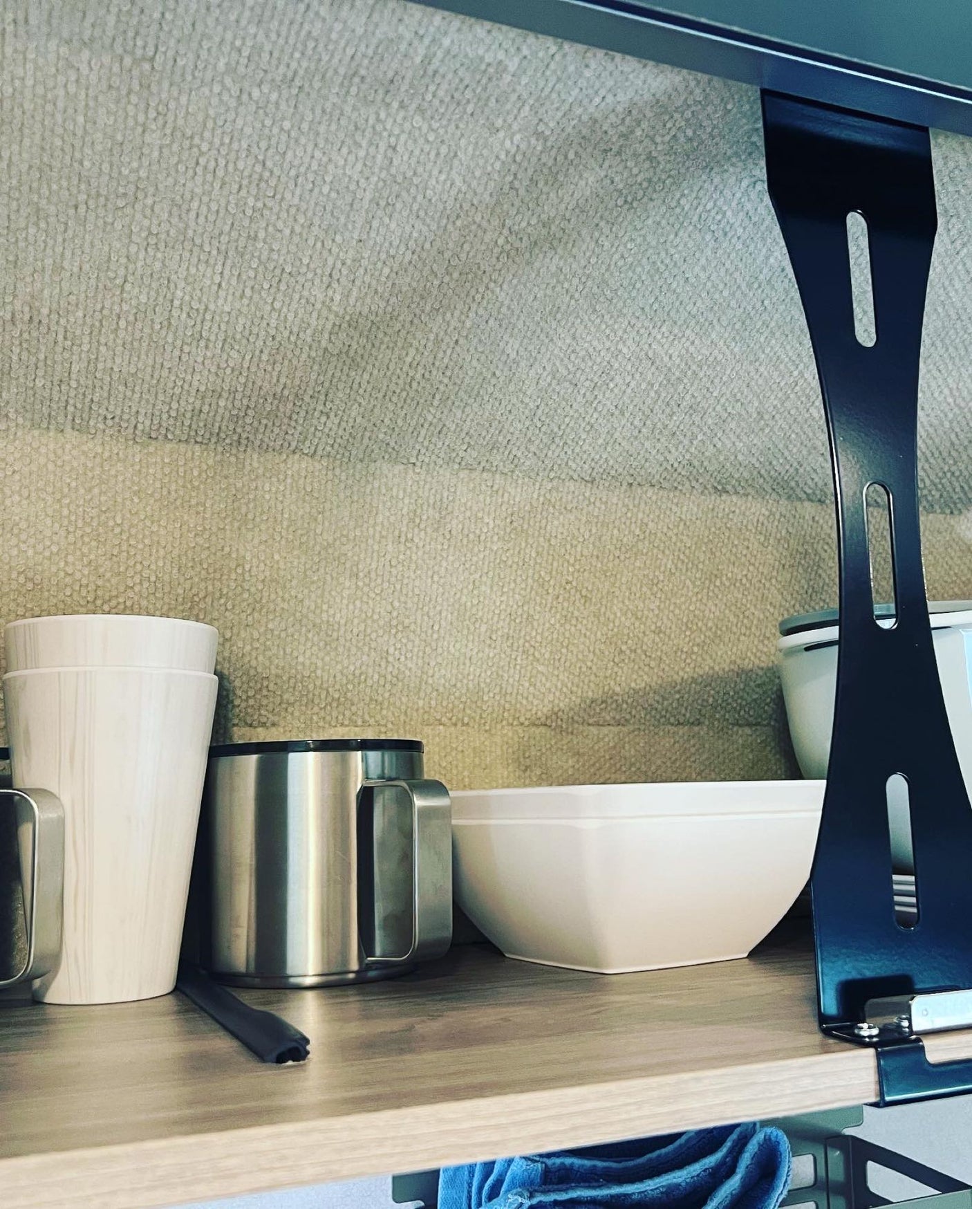 RV rental interior showing kitchen storage. Cups, a mug, and a bowl neatly on a shelf with textured walls, typical for camper living.