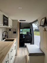 Bright, modern RV rental interior with a kitchenette featuring white cabinets, wood counters, and a cozy bench area.
