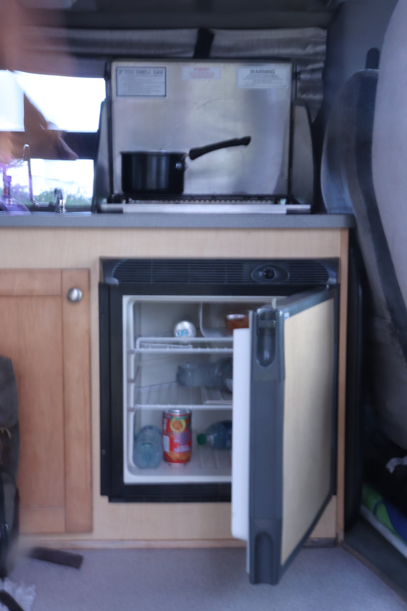 RV rental's compact kitchen: open fridge with drinks/food and a stove. Perfect for road trips. — photo 20