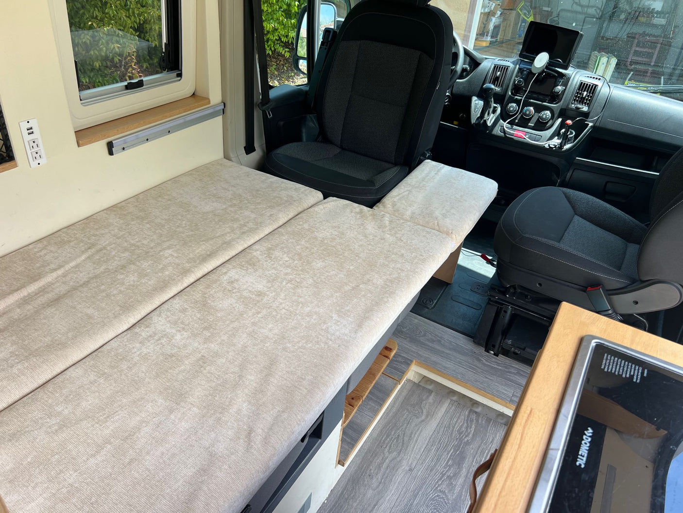 Explore this RV rental's cozy interior: bed, window, and driver's area with dashboard and swivel seat.