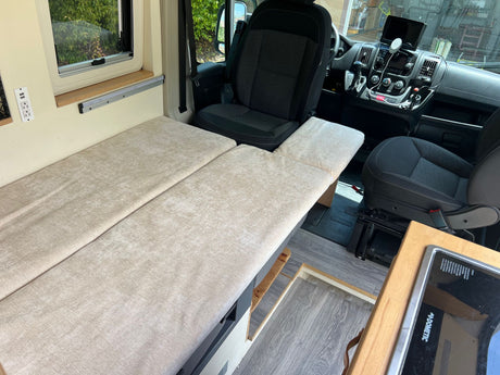 Explore this RV rental's cozy interior: bed, window, and driver's area with dashboard and swivel seat.