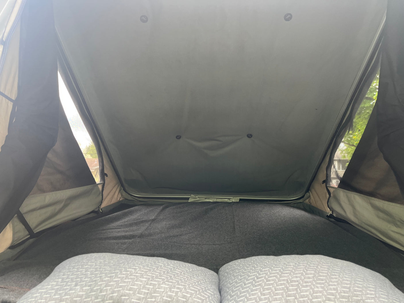 Looking up at the cozy sleeping area within an RV rental rooftop tent, featuring pillows and soft bedding.