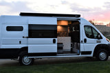 This white camper van, available for rv rental, shows its custom interior with a mobile kitchen, perfect for van life adventures.